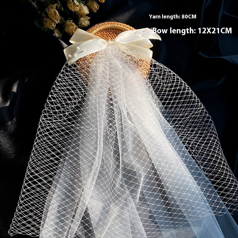 Bow veil with white tulle and cream ribbon bow displayed over a wicker base, wedding decor