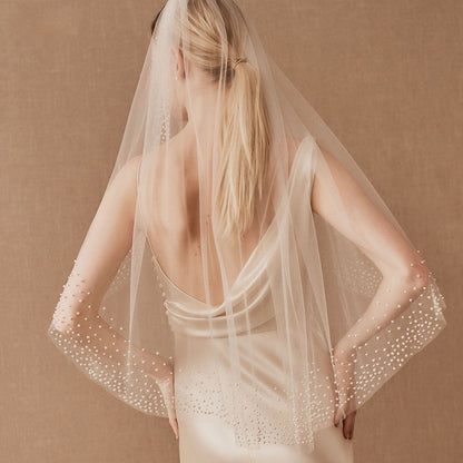 Beading bridal veil in sheer ivory mesh with pearl beads, draped over the back of a wedding gown.