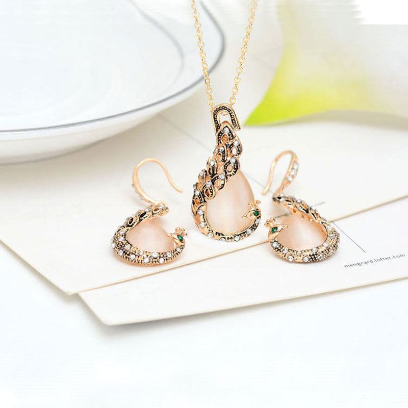 Bridal peacock gem necklace and earrings set; gold-tone with pink teardrop stones, clear crystals, and green accents.
