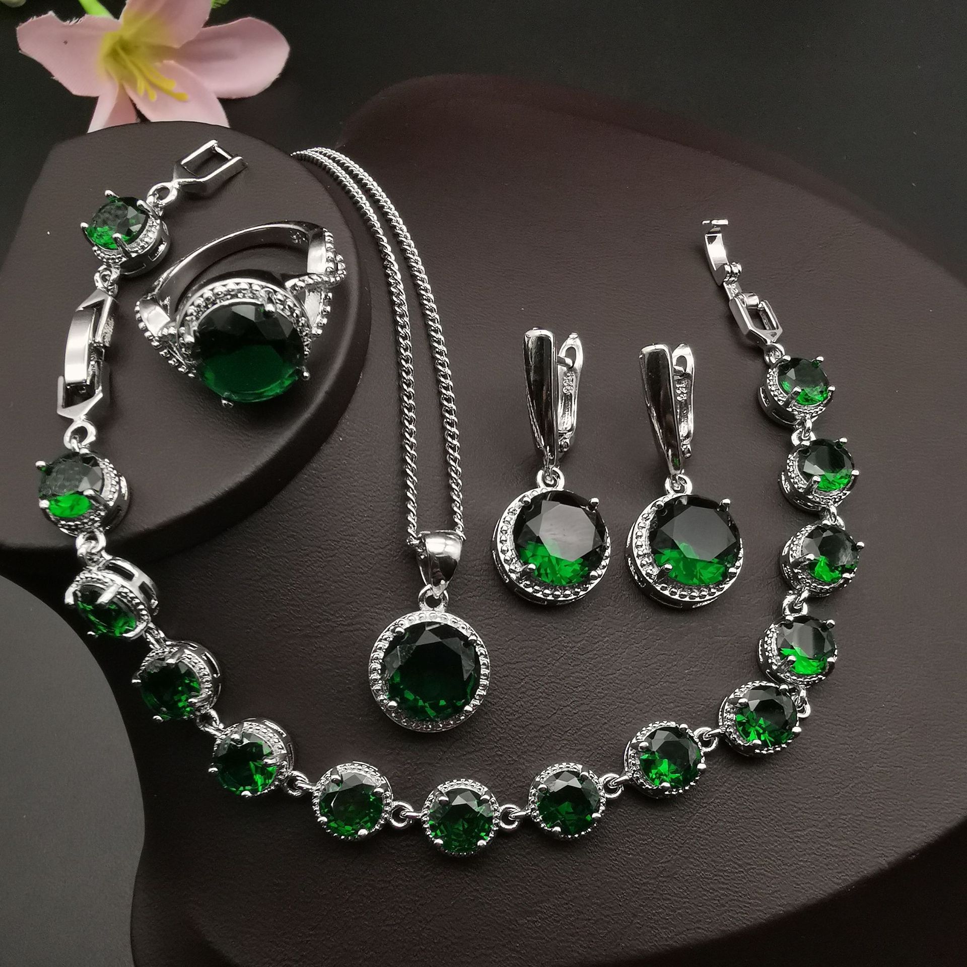 4-piece jewelry set with emerald-green round stones and diamond halos; includes necklace, bracelet, ring, and earrings.