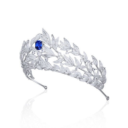 Silver tiara crown with intricate leaf design, blue sapphire centerpiece and shimmering zircon inlays.