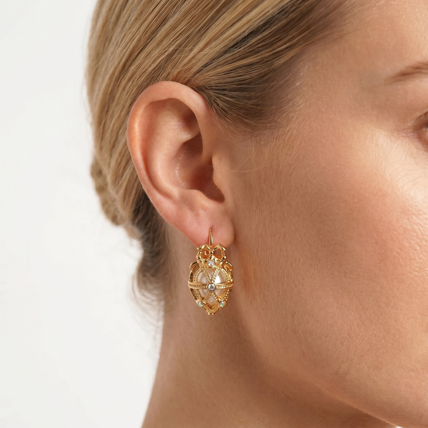 Gold earrings featuring a hollow Easter egg bow pendant with crystal accents, worn on the ear.